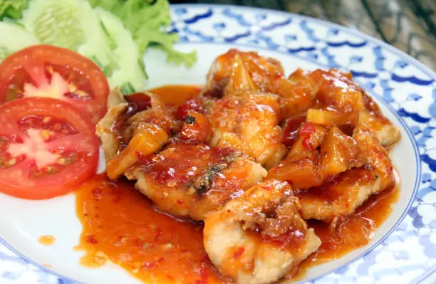 Fried fish cutlet in sweet and sour sauce with a side of fresh tomatoes and cucumber
