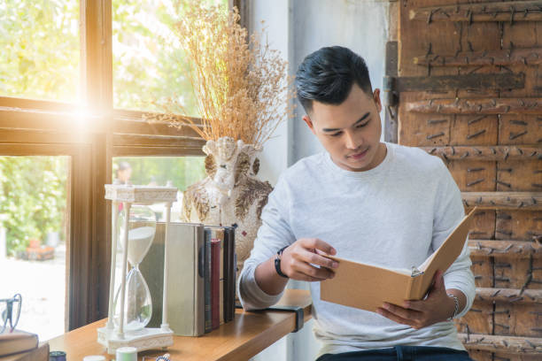 istock Asian boy reading a book sitting on a chair by the window. 900313834