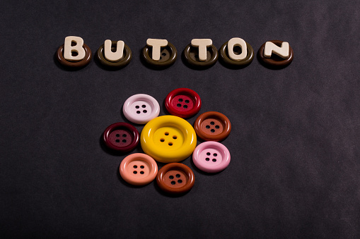 Word button in wood letters on black background with many colored buttons