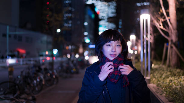 istock Young woman standing on a sidewalk at night 900325678