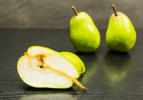 istock Cut half a pear on a wooden dark table. 900400114