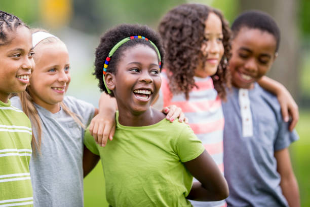 Class Pictures A group of elementary school kids are outside on a summer day. They are embracing and smiling while taking a group photo. preadolescents stock pictures, royalty-free photos & images