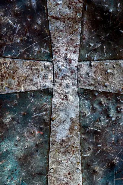 Detailed close-up photo of a christian cross symbol on a rusty battered medieval armor.
