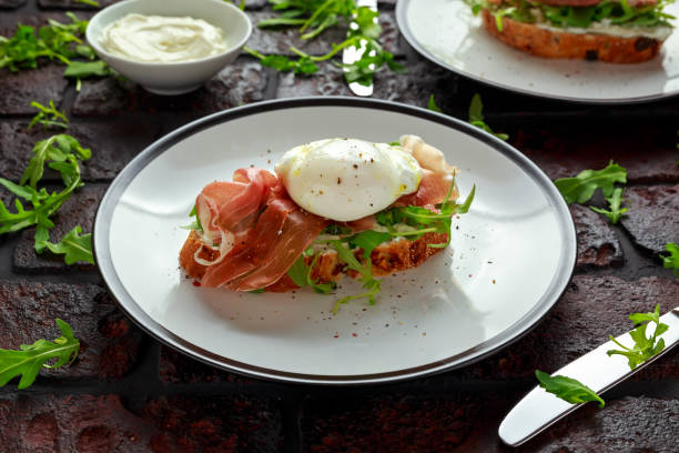 istock Bruschetta with cream cheese, wilde rucola, parma ham and poached egg served on white plate 900427980