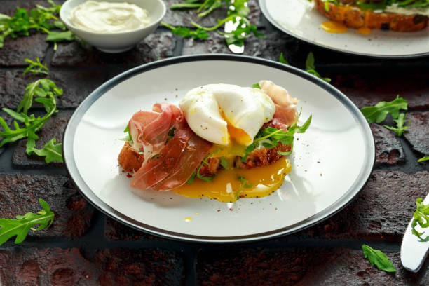 bruschetta with cream cheese, wilde rucola, parma ham and poached egg served on white plate - poached egg imagens e fotografias de stock