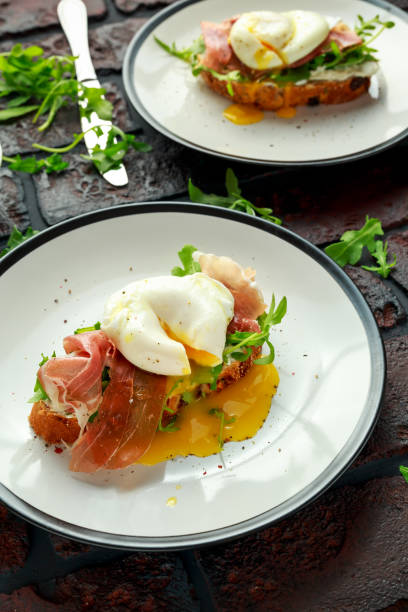 istock Bruschetta with cream cheese, wilde rucola, parma ham and poached egg served on white plate 900428028
