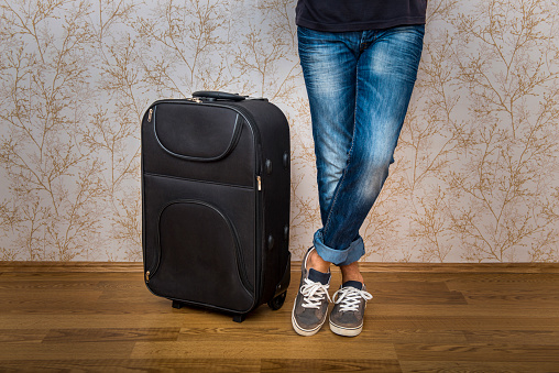 Low section view of young man standing near the suitcase at home. Horizontal composiiton. Image taken with Nikon D800 and developed from Raw format.