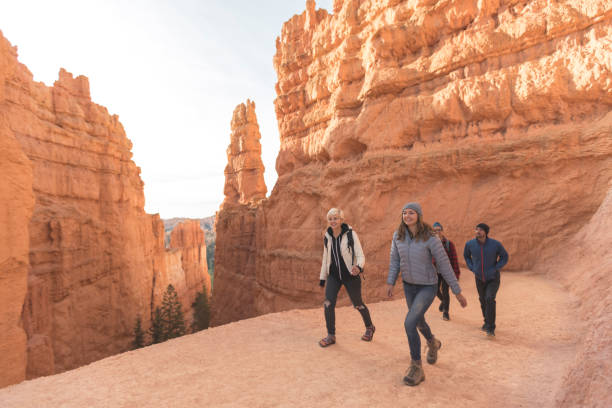 A quartet of friends in their 20s head out on a day hike through the stunning cliffs and landscapes of Utah's Bryce Canyon National Park. Two females are in front, followed by their boyfriends. They are surrounded by towering, jagged pinnacles of rocks and ridges.