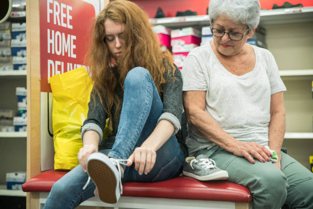 la plata-haired mujer senior activa de 65 años de edad y su nieta adolescente infeliz compras zapatos en la tienda de venta por menor de ropa - 13 14 years teenager 14 15 years child fotografías e imágenes de stock