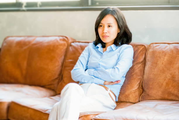 istock A Japanese woman sits deep on the sofa. Staring at something serious. 900517902