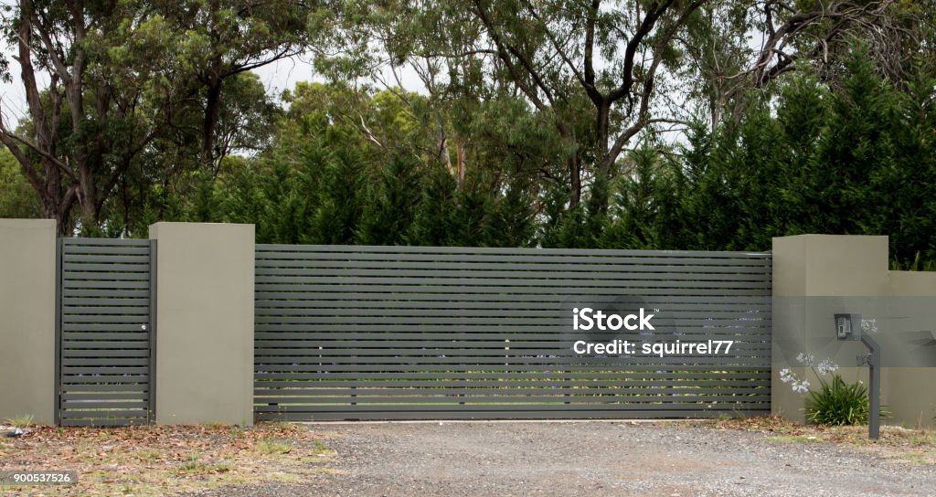Metal driveway entrance gates set in brick fence leading to rural property with eucalyptus trees in background Gate Stock Photo