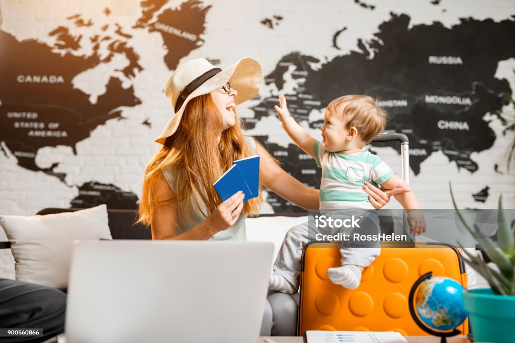 Happy family at the travel agency office Happy and playful woman with baby boy sitting at the travel agency office with beautiful map on the background ready for a summer vacation Travel Stock Photo