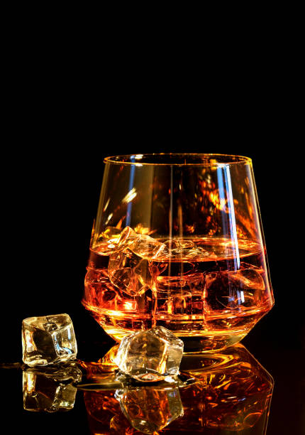 Whiskey with ice in glass on black background