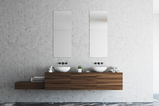 Concrete bathroom interior with a marble floor, a double sink with a wooden shelf and two narrow vertical mirrors. 3d rendering