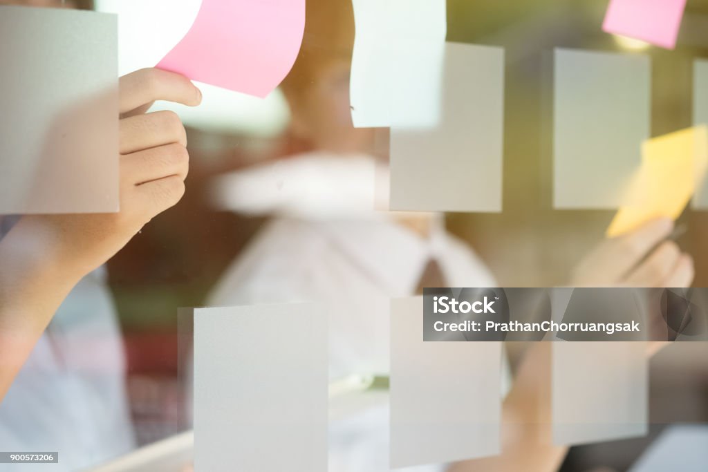 Gli uomini d'affari creativi che leggono note adesive sulla parete di vetro con il collega che lavora usano le note post it per condividere idee che discutono e lavorano in team, concetto di brainstorming. Colpo da primo piano. - Foto stock royalty-free di Muro