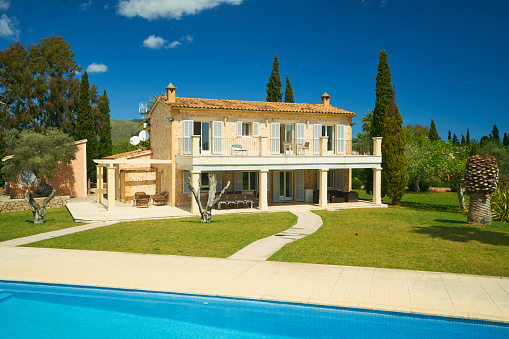 typical spanish finca house with well kept garden and big swimming pool on sunny day with blue sky