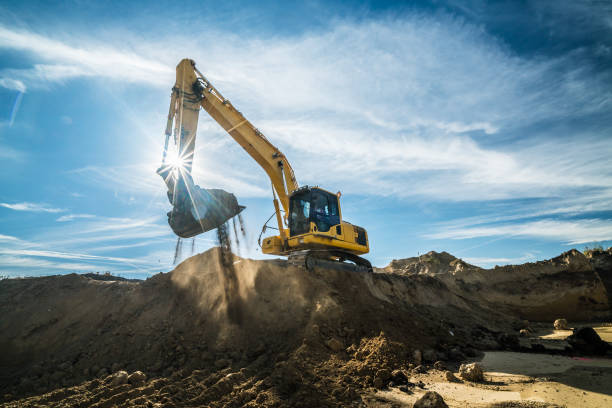 Construction - digger working at building site on sunny day yellow digger digging excavation for new houses on a building site in backlight, high noise from recoverd shadows bulldozer photos stock pictures, royalty-free photos & images