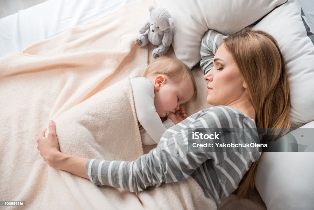 Little family reposing at home Top view of peaceful mother and cute child lying on double bed. They are sleeping together with tranquility Mother Stock Photo