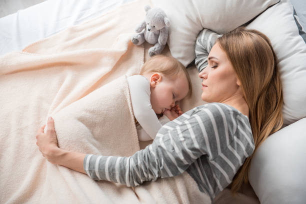 Little family reposing at home Top view of peaceful mother and cute child lying on double bed. They are sleeping together with tranquility sensory perception photos stock pictures, royalty-free photos & images
