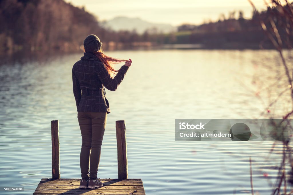 Jeune femme se tient sur un pont de bois à un lac, le fond de la nature avec les montagnes - Photo de Adulte libre de droits