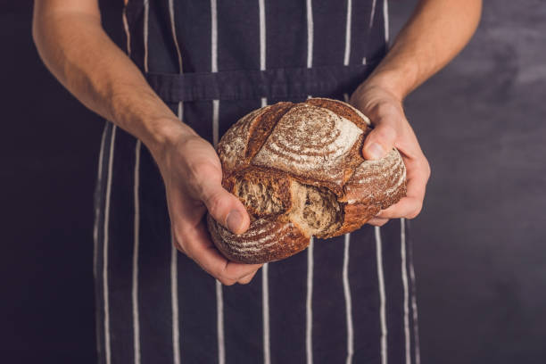 istock Baker man holding homemade rustic wheat bread in hands. Selective focus 900610800