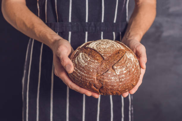 istock Baker man holding homemade rustic wheat bread in hands. Selective focus 900610810