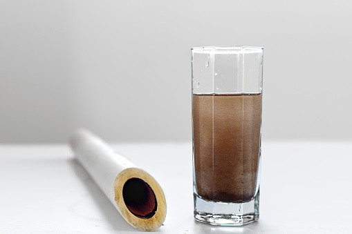 Dirty water in a glass and in a plastic pipe on a white table and a light background. Concept of clarification of water