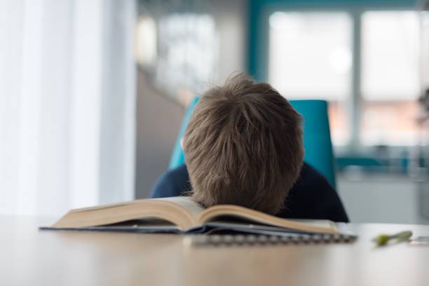 テーブルで宿題をして疲れている 8 歳の少年 - learning boredom studying child ストックフォトと画像