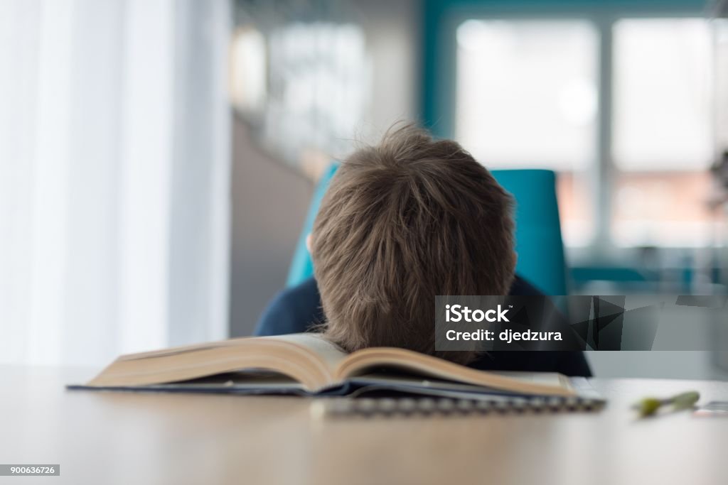 Tired 8 years old boy doing his homework at the table Tired 8 years old boy doing his homework at the table. Child reading a book at the desk. Child Stock Photo