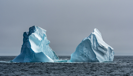 Two massive icebergs floating in the Southern Ocean in Antarctica showing the weathered shapes resulting from wind and sea erosion