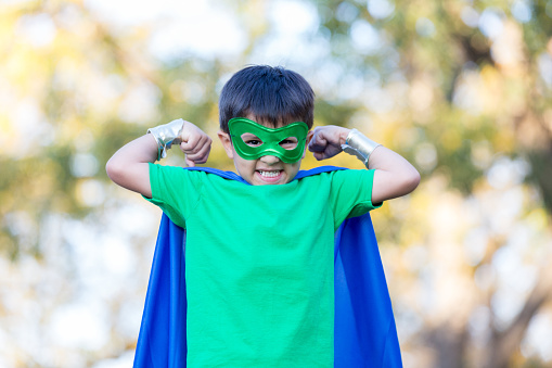 Young male superhero flexes his muscles and makes a face. He is wearing a mask and cape.