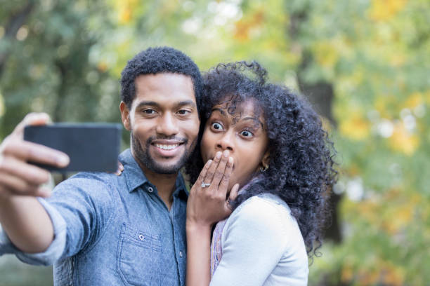 istock Young couple pose for silly engagement selfie outside 900665040