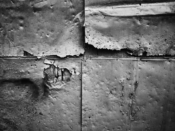 Close-up of a dark wall surface with rough texture and visible imperfections. The worn and gritty appearance creates a moody, industrial, and aged atmosphere.