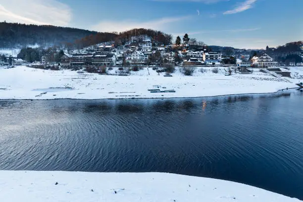 Evening view over lake Rursee to the village of Rurberg with snow in winter in the Eifel, Germany.