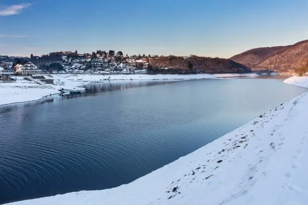 Evening view over the reservoir lake Rursee to the village of Rurberg with snow in winter in the Eifel, Germany.