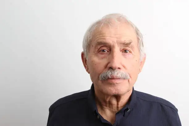 An old man looking at camera with a serious facial expression on white background