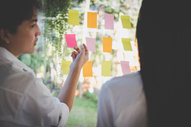 istock man & woman discussing creative idea with adhesive notes on glass wall at workplace. Sticky note paper reminder schedule at office. business, brainstorming, creativity concept 900723844