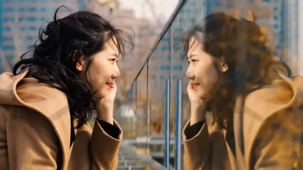 Beautiful Chinese girl looking at her mirror image in glass.