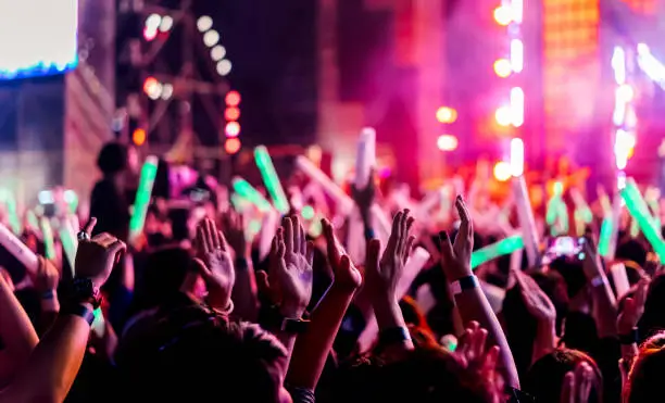 Photo of Crowd clap or hands up at concert stage lights and people fan audience raising hands silhouette with spotlights glowing effect in the music festival rear view