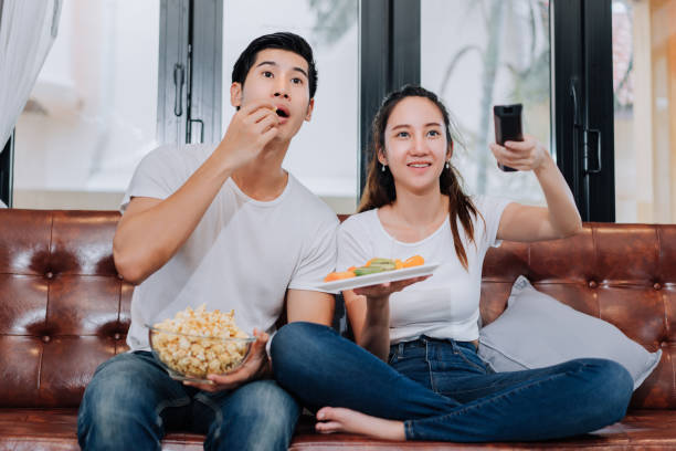 couple ensemble je regarde la télévision spectacle film horor, action, réaction drôle comédie assis relaxation manger les fruits et les pop-corn sur canapé canapé confortable dans la salle de séjour à la maison - horor photos et images de collection