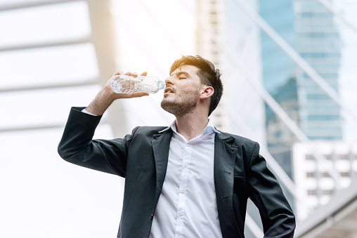 Tired sale man concept. Tired direct sale man resting and drinking water after a hard day of work. Taken outdoor, business team spirit, and refreshing ideas concepts.