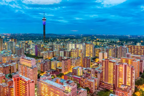 Johannesburg cityscape in the evening dusk across Hillbrow residential suburb of towering apartments. The iconic Hillbrow communication tower seen in the midst. Johannesburg is one of the forty largest metropolitan cities in the world, and the world's largest city that is not situated on a river, lakeside, or coastline. It is also the source of a large-scale gold and diamond trade, due being situated in the mineral-rich Gauteng province.