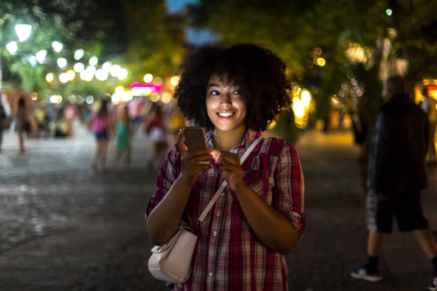 istock Smiling woman using smart phone on street at night 900799708
