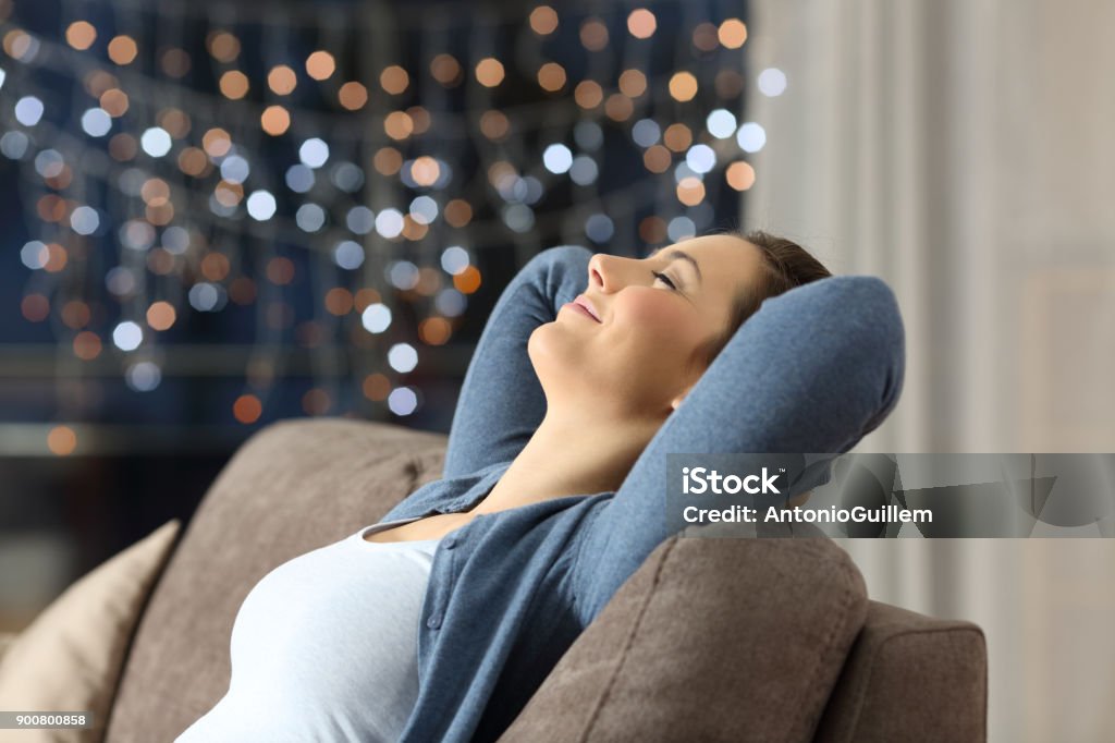 Woman resting on a couch in the night at home Side view portrait of a relaxed happy woman resting sitting on a couch in the night at home Vacations Stock Photo