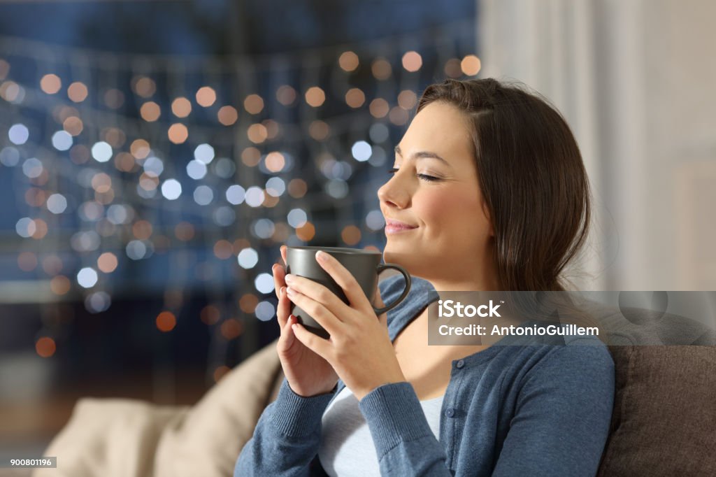 Woman relaxing drinking coffee in the night at home Portrait of a satisfied woman relaxing drinking coffee in the night sitting on a couch in the living room at home Tea - Hot Drink Stock Photo