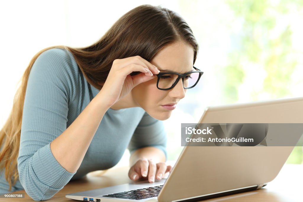 Woman with eyesight problems to read on line content Woman with eyesight problems trying to read on line content in a laptop at home Myopia Stock Photo