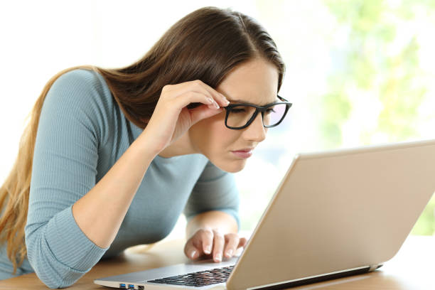 Woman with eyesight problems to read on line content Woman with eyesight problems trying to read on line content in a laptop at home myopia stock pictures, royalty-free photos & images