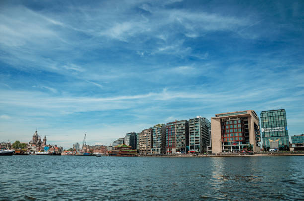 порт, церковные башни и современные здания на берегу канала и голубое небо в амстердаме. - harborage стоковые фото и изображения