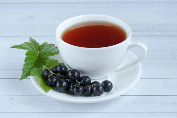 Cup of tea and black currant on a wooden background