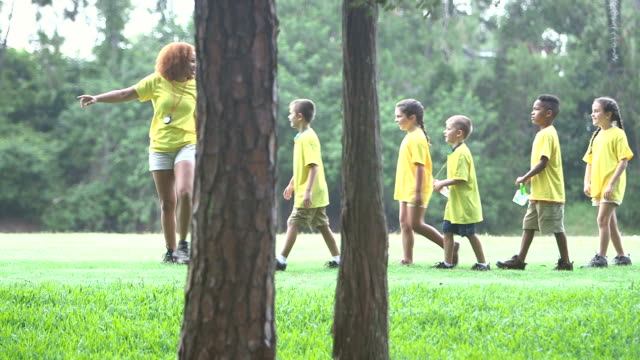 Camp counselor with children in park walking single file